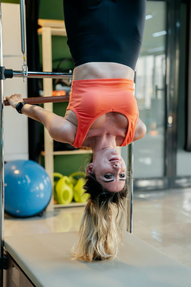 Adult woman performing an upside down pilates exercise on equipment in a gym setting.